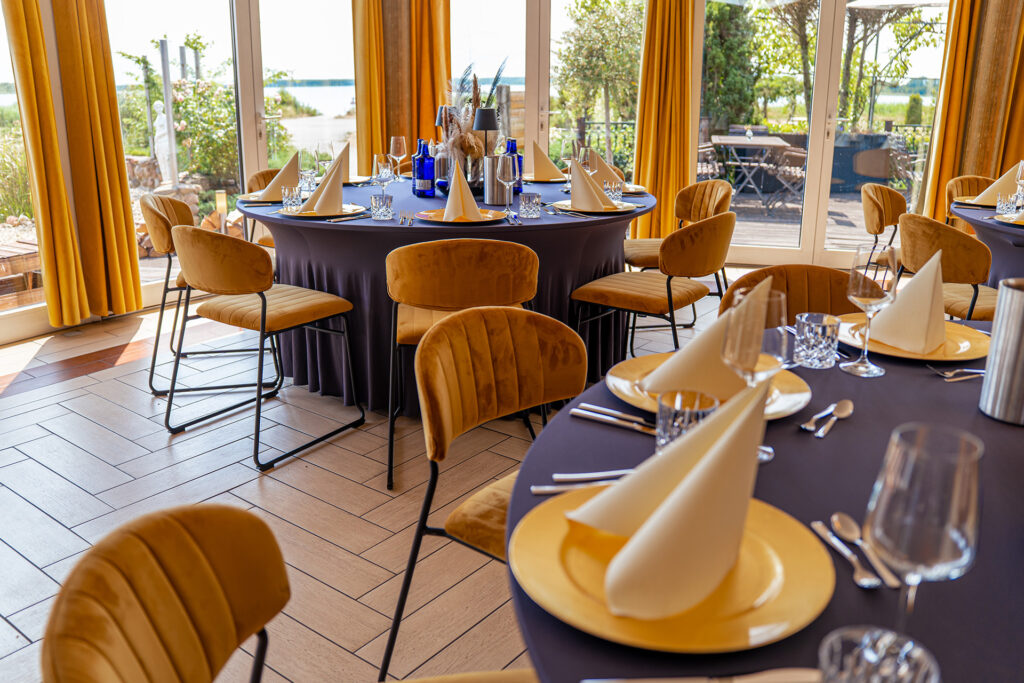 Veranstaltungsraum der Bernstein Events Location am Goitzschesee mit goldenen Stühlen und runden Tischen, im Hintergrund der See